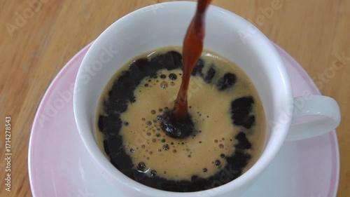Close-up moment hot coffee is poured into white ceramic cup, swirling patterns on the surface evoking warmth and energy.