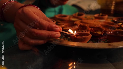 An Indian woman in traditional attire lights clay diyas during Diwali celebrations at home, surrounded by marigold flowers and festive decorations