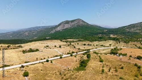 Cinematic aerial drone video of a car on a lonely road driving through the vast Dinaric Alps landscape