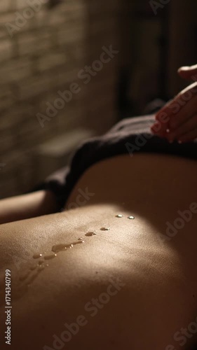 masseuse pours massage oil on back and gives back massage. close-up. dim light