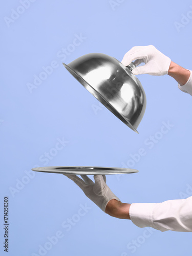 Foto Hands lifting silver cloche from tray on blue background