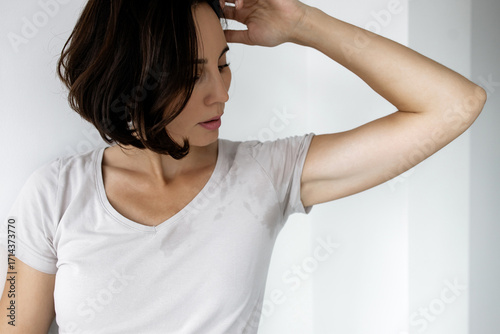 Woman checking sweat stain under armpit on her t-shirt, concept of excessive sweating, body odor and hyperhidrosis problem in adult female 