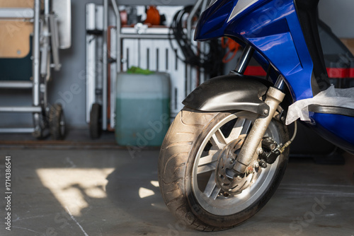 Close-up of a blue scooter front wheel with brake disc in a garage, transportation and urban mobility concept.