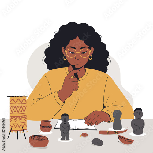 An artist contemplates tribal artifacts, holding a pen above an open notebook on a table