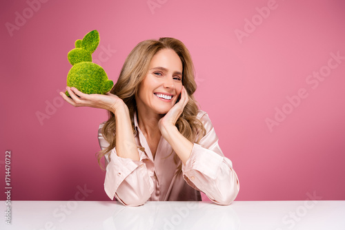 Charming mature woman holding a decorative green bunny displaying elegance and joyful expression