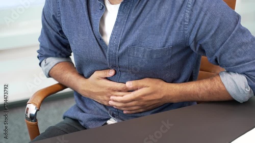 Close up. Male hands holding massaging stomach. Businessman in casual shirt feels stomach pain sitting at workplace in business office. An unhealthy man suffers from gastritis, poisoning or bloating
