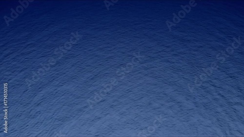 An aerial view of a vast, deep blue water surface, featuring subtle, rhythmic ripples and gentle waves. The rich, dark blue color evokes a profound sense of depth, tranquility, and serene mystery. The