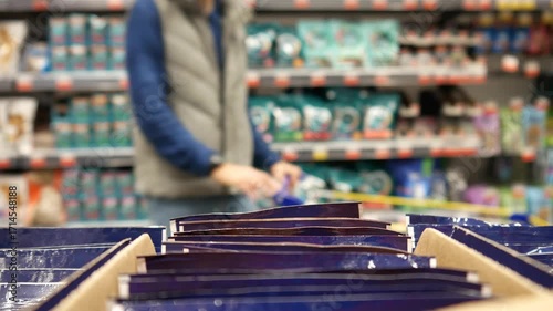 A male customer with a shopping trolley takes three packs of wet animal food in a pet store