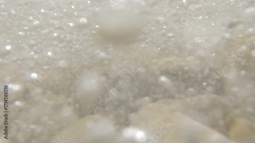 Crystal clear waves splashing on the pebble beach and hitting the camera. Close-up. Slow motion.