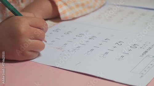 Young student doing math homework with pencil on worksheet showing addition problems and learning progress