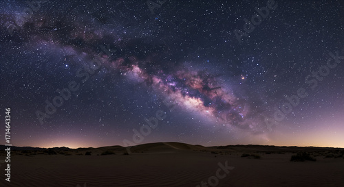 The Milky Way galaxy arcs majestically across a star-filled night sky above a serene desert landscape with rolling dunes.