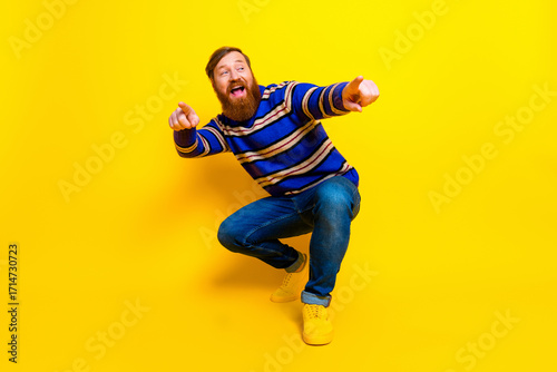 Quadro em tela Cheerful bearded man in casual striped sweater posing happily against vibrant ye