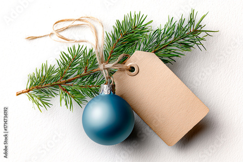 A blue Christmas ornament with a natural pine sprig and a kraft tag, tied with twine, on a light gray background.