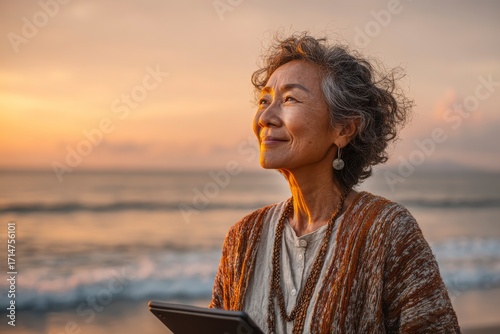 Reflective Senior Woman at Sunset on Beach Holding Tablet Device