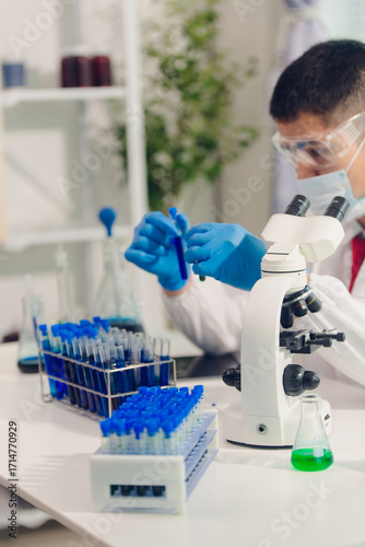 medical or scientific researcher researching and experimenting Multi-colored solution, vial and microscope In the laboratory or in the laboratory by wearing blue gloves and white clothing completely.