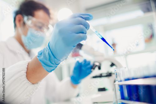 medical or scientific researcher researching and experimenting Multi-colored solution, vial and microscope In the laboratory or in the laboratory by wearing blue gloves and white clothing completely.