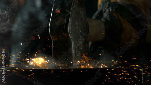 Close-up of blacksmith forging glowing hot iron on anvil with flying sparks