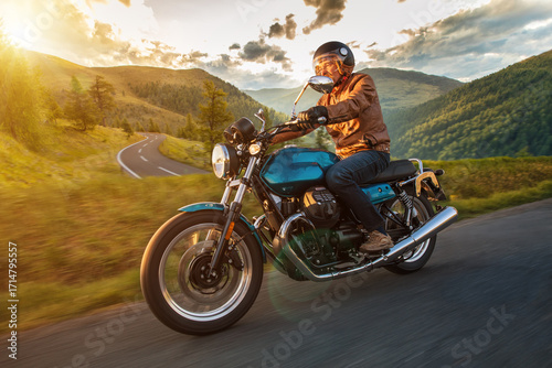 Driver riding motorcycle on empty road during sunset, spring mountains