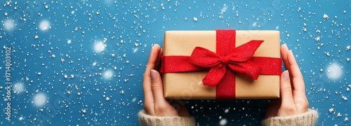 Holding a Wrapped Gift With a Red Bow Against a Snowy Blue Background in Winter