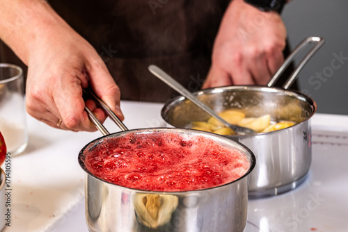 Hands of a chef holding a stainless steel pot with bubbling red sauce, while another pot with pasta simmers on the stove, showcasing culinary skills and vibrant cooking process