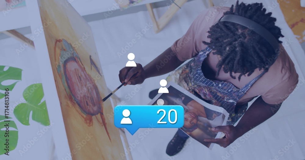 Naklejka premium Painting artist wearing apron applying color to canvas on easel in studio with brush and reference