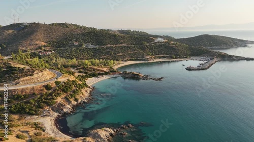 High-resolution aerial drone image showcasing a picturesque beachfront resort scene. Neatly arranged white umbrellas and lounge chairs line the golden sandy shore, while colorful hotel buildings with 