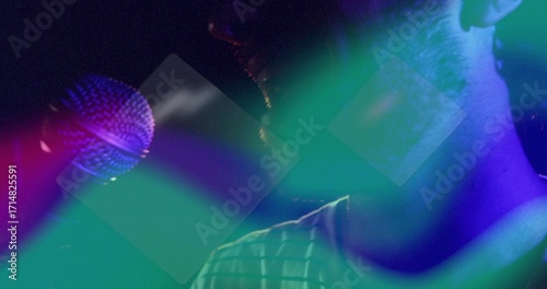 Performing singer wearing striped shirt singing under neon haze at nightclub, with handheld mic