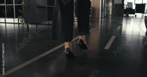 Close-up of a woman walking in black high heels along a shiny polished office hallway with modern design and natural light reflecting on the floor