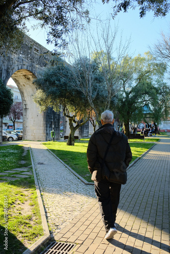 Sunny city park with olive trees green lawn walking paths and historic stone aqueduct arches in background Lisbon Portugal leisure landscape no people and candid walker variations. High quality photo