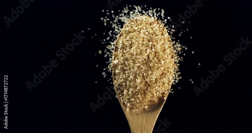 Slow Motion of Golden Brown Cane Sugar Crystals Falling from Wooden Spoon in Slow Motion on Black Background for Food, Cooking and Sweetness Concept at 1000 fps.