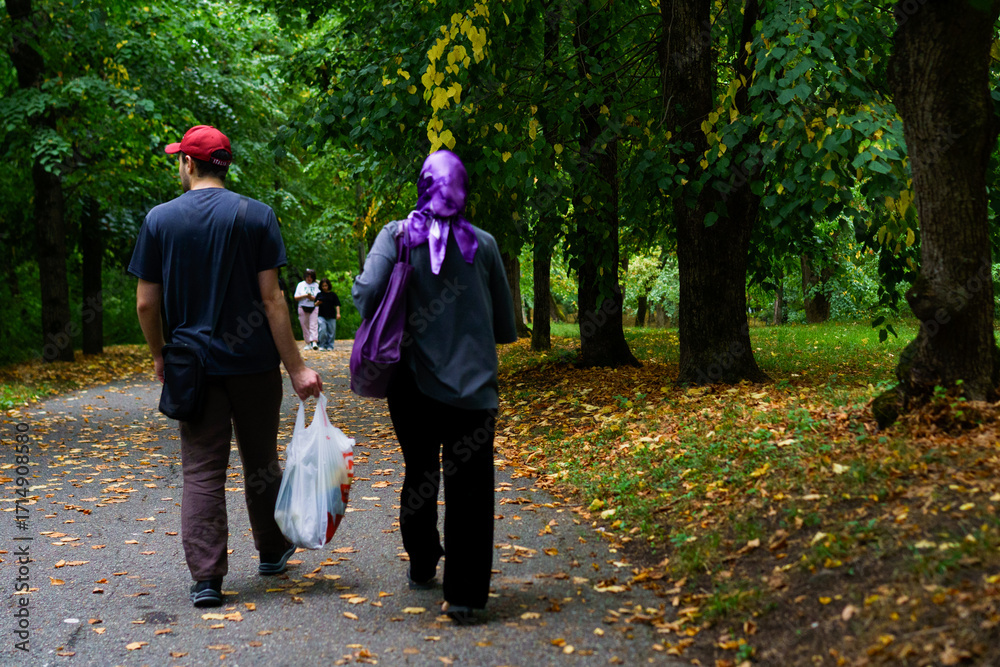 Fototapeta premium Couple st Rolling through park adorned with autumn leaves, enjoying a peaceful leisurely walk in nature
