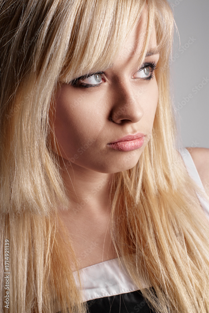Naklejka premium Close-up portrait of young woman with blonde hair and thoughtful, displeased gaze. Her eyes look off into the distance. Simplistic background highlights her features.