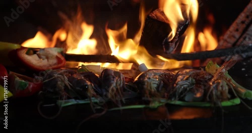 Langoustines with vegetables on the grill against a backdrop of flames, slow motion