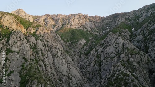 Drone tilt reveals a highland ridge above a limestone gorge in Uzbekistan with green slope, gravel ribbon and distant pass. Golden hour brightens the crest and carves shadow for a cinematic landscape