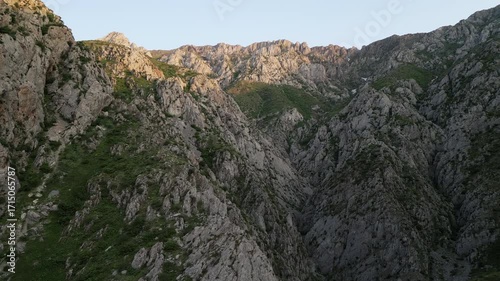 Aerial view drifts across the Chimgan range in Tashkent region, tracing a deep canyon with jagged walls, scree slope and hidden gully. Early sun skims the crest and adds depth for travel and nature