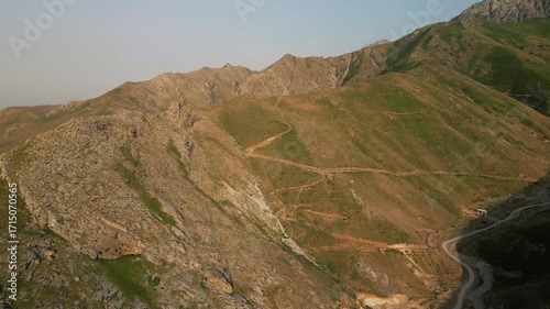 Mountain valley in Surkhandarya, Uzbekistan, filmed at golden hour from a drone. Rugged Baysuntau ridges, winding dirt road, warm light and long shadow convey scale, remoteness and adventure