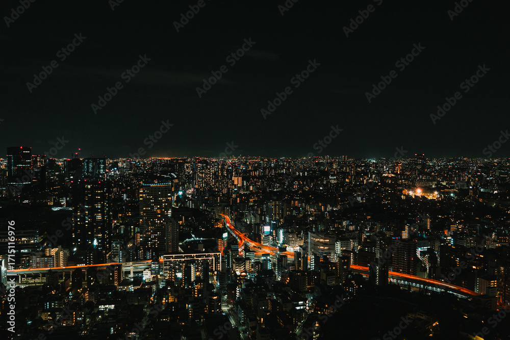 Fototapeta premium A high-angle view of a bustling city at night, showcasing the vast expanse of lit buildings and highways with distinct glowing lines of traffic