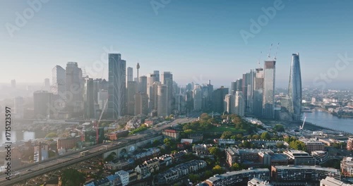 Australia, Sydney: Aerial view of Sydney Harbour Bridge and city skylines skyscrapers reflecting in water at misty sunrise, Barangaroo Reserve and wharves in foreground. Drone flight footage panorama