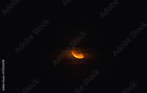 A glowing half moon, a warm orange light in the dark sky, partially obscured by the faint cloud.