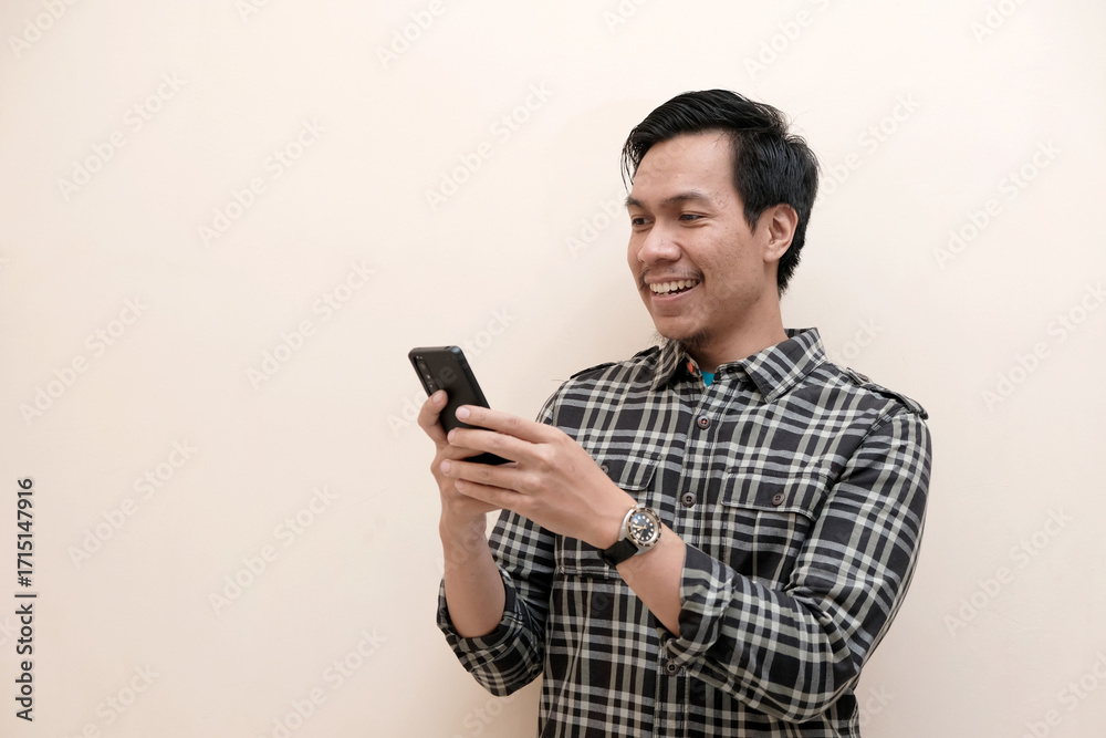 Fototapeta premium Southeast Asian man wearing flannel shirt standing and smiling expression happy with holding mobile phone, on white isolated background.