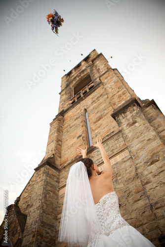 Bride Tossing Bouquet of Flowers Backwards in Front of Old Church Bell Tower