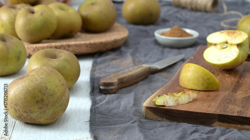 A half-cut apple and a small wedge, both lightly dusted with cinnamon, rest on a rustic wooden cutting board. The scene is set with a knife, twine, and a bowl of cinnamon, suggesting a cozy, autumnal 