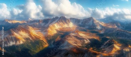 Sunlit rugged mountain range with sharp peaks under a partly cloudy blue sky, highlighting autumn colors in valleys and rocky slopes