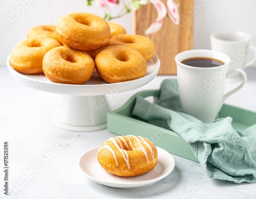 Original donuts arranged on a white porcelain plate, with a serving of black coffee on a tray and a green cloth 