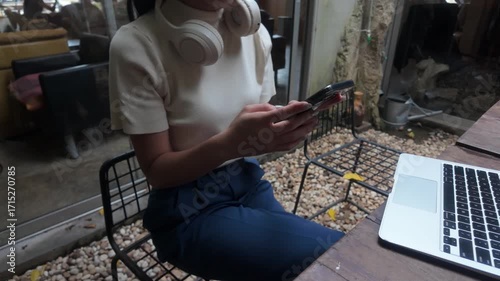 Young businesswoman with headphones texting on her mobile phone. A modern entrepreneur working remotely from a cafe with a laptop on the table