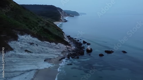 Coastal scenery at twilight, with gentle waves lapping the shore, captured from a high vantage point.