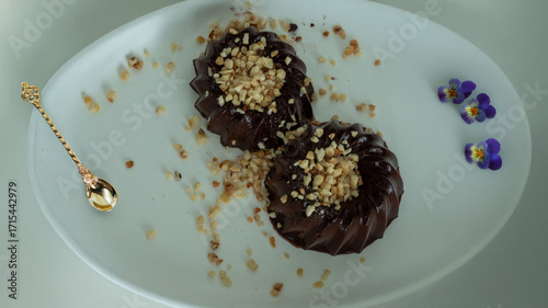 Two chocolate jellies topped with chopped nuts on a white plate, decorated with edible flowers.