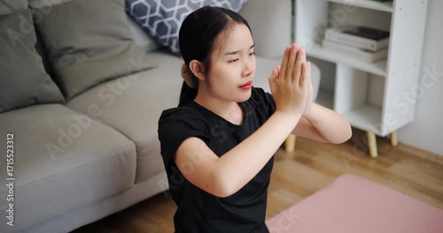 Handheld high angle view shot, Calm Asian woman is enjoying yoga in lotus position on a yoga mat in living room at home. Healthy Lifestyle Concepts