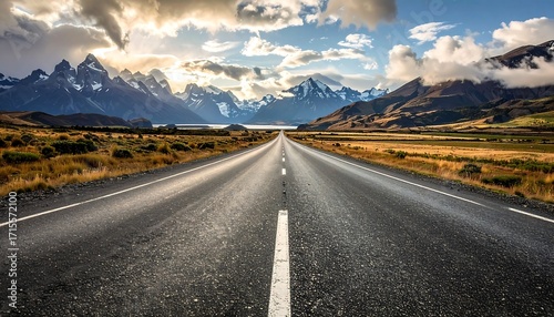 A paved road stretches out into a vast landscape, flanked by mountains and a dramatic sky.
