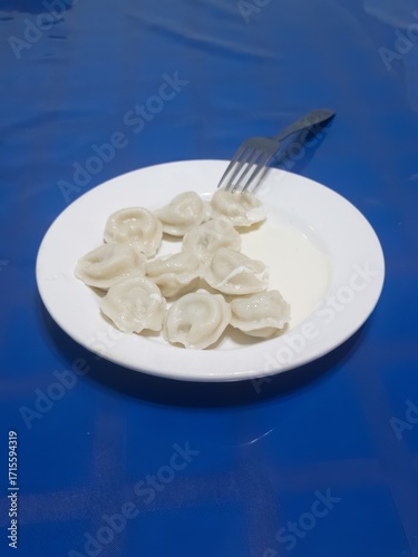A Russian dish - a plate of vareniki with cottage cheese and sour cream on a table covered with a blue tablecloth